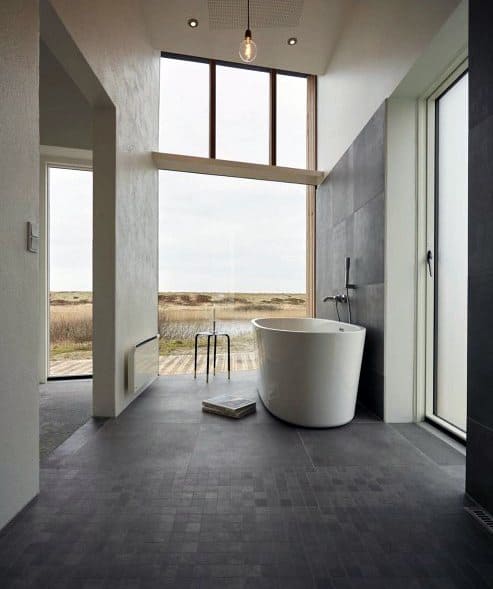 White freestanding tub in modern bathroom with large windows and countryside views.