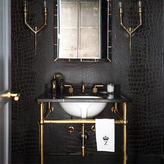 Luxurious black bathroom with gold fixtures, ornate mirror, and white sink basin.