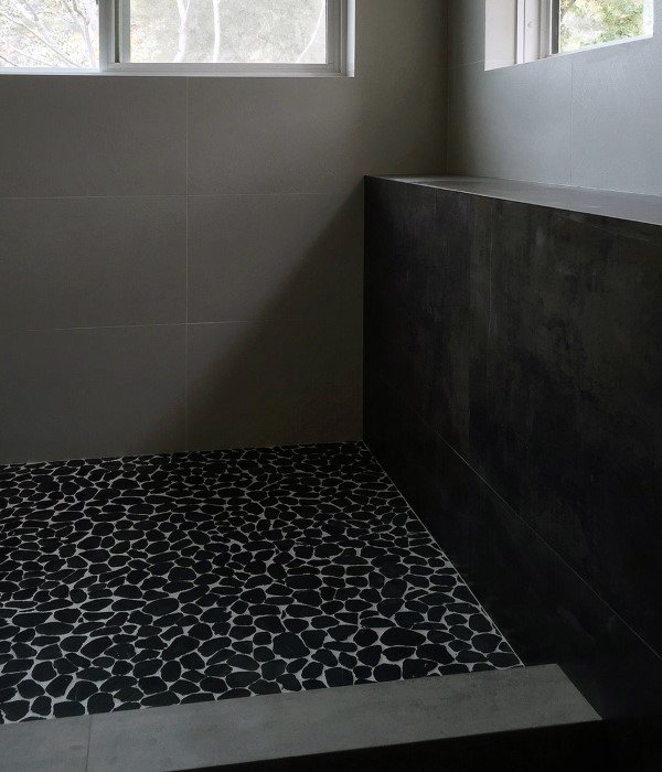 Modern shower with black pebble stone floor tiles and minimalist dark walls.