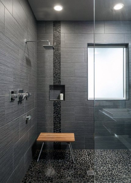 Minimalistic modern shower with grey textured tiles, pebble stone floor, and wooden bench.