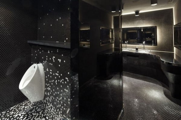 Modern black bathroom with small hexagonal tiles and a white urinal against mosaic wall.