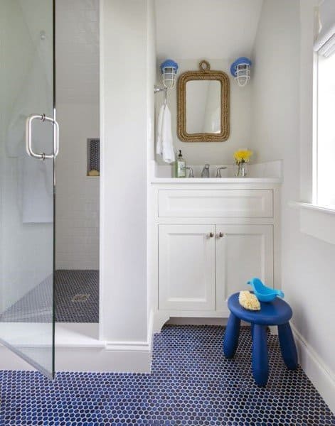 Children's bathroom with blue hexagonal floor tiles, white vanity, and glass shower.