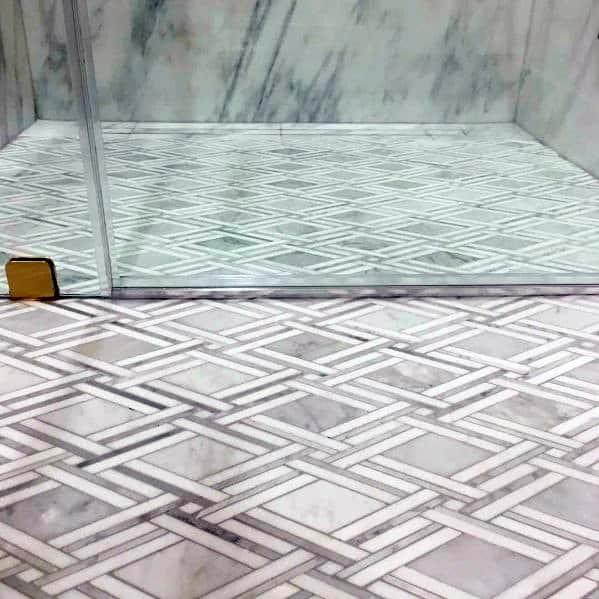 Patterned marble bathroom floor tiles with geometric design inside a glass shower.