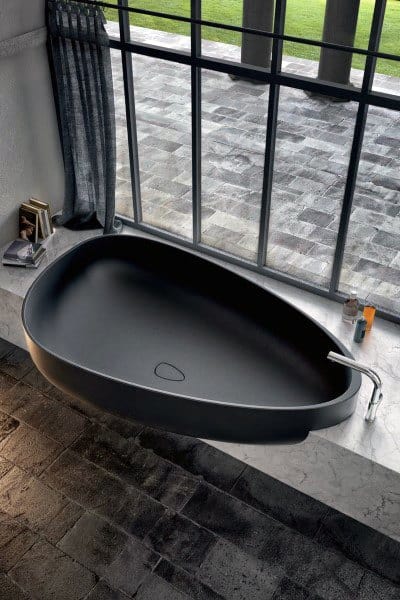 Modern black stone bathtub by large window with natural light.