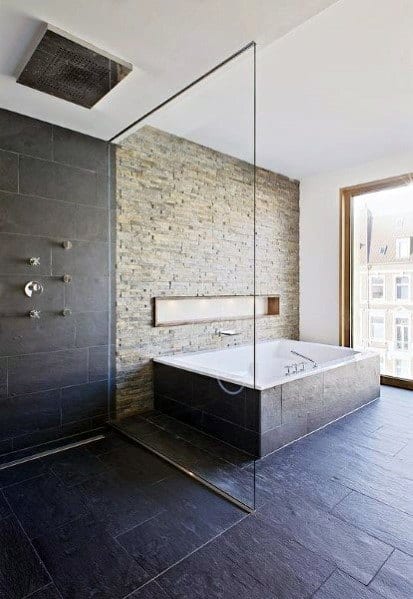 Modern bathroom with slate tiles, glass shower, and large bathtub by stone accent wall.