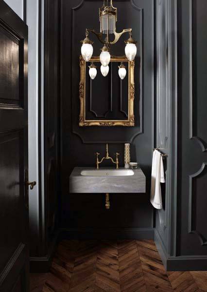 Elegant black bathroom with gold-framed mirror, chandelier, and herringbone floor.