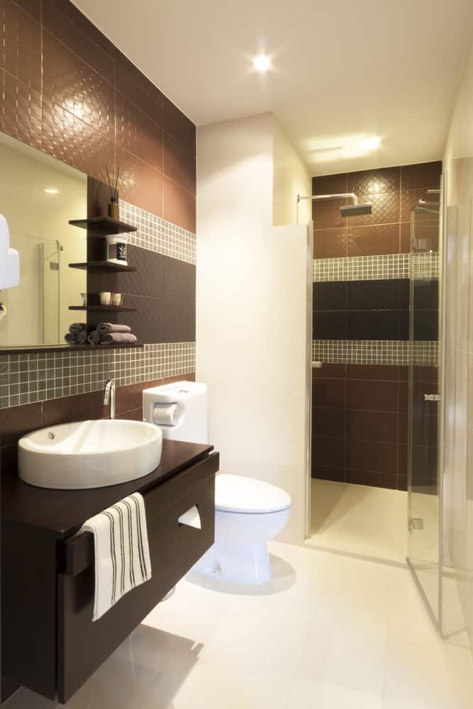 Modern bathroom with dark tiled walls, glass shower, and sleek vanity.