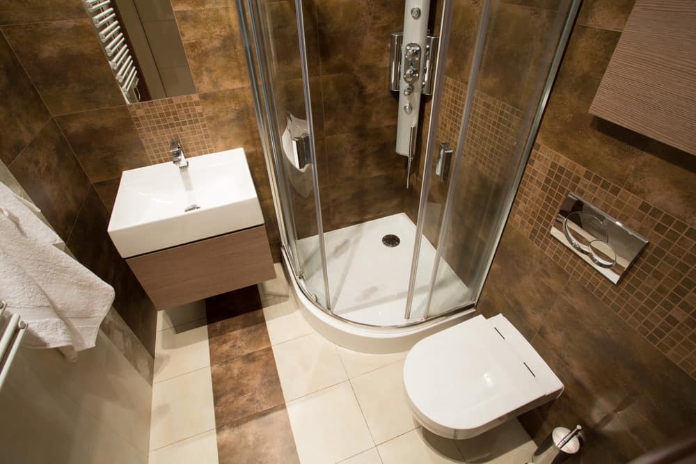 Compact bathroom with brown tiles, corner shower, and wall-mounted vanity.