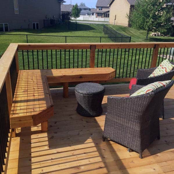 Wooden deck with a built-in bench, a wicker chair with cushion, and round table, overlooking a grassy backyard