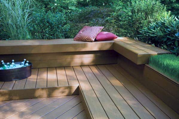 Wooden deck with bench seating, red cushions, and a tub of drinks surrounded by lush green foliage