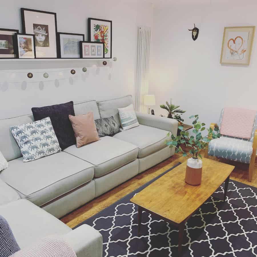 Cozy living room with a gray sofa, wooden coffee table, and patterned rug; wall art and potted plants add decor