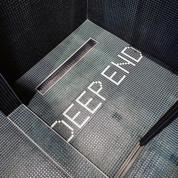 Shower floor with small black tiles and "Deep End" inlaid white lettering near drain.