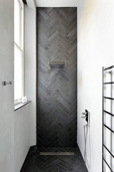 Small shower with dark chevron-patterned tile and built-in shelf.