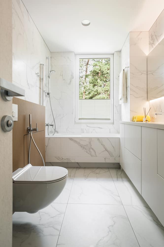 Bathroom with marble walls, floating vanity, and a window providing natural light.