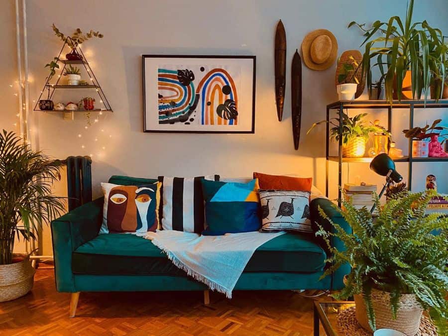 Cozy living room with a green sofa, colorful cushions, wall art, plants, and warm string lights