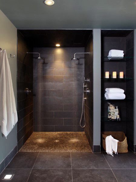 Shower with two showerheads, dark tiled walls, and pebble stone floor.