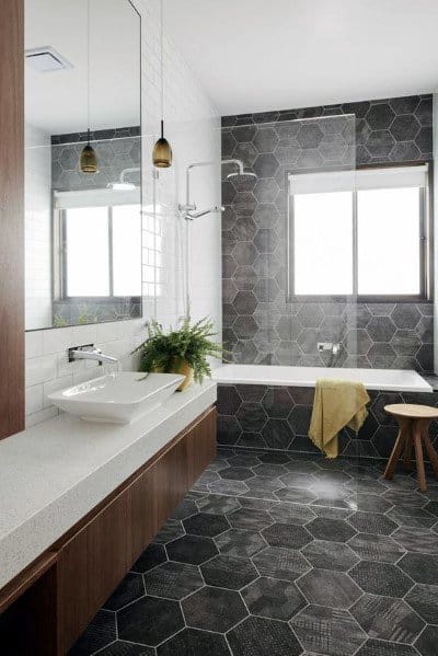 Modern bathroom with black hexagonal tiles, white vanity, and bathtub with glass partition.