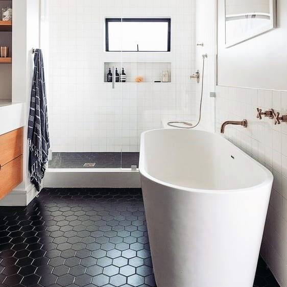 Bathroom with freestanding tub, black hexagonal floor tiles, and glass-enclosed shower.