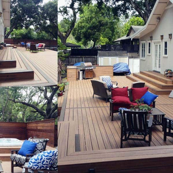 Wooden deck with bench seating, cushions, plants, and a hot tub under trees beside a house