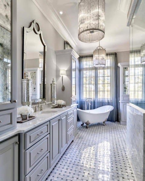 Elegant bathroom with freestanding bathtub, double chandeliers, and mosaic floor tiles.