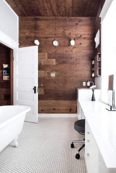 Modern bathroom with wood panel feature wall, white freestanding tub, and hexagonal floor tiles.