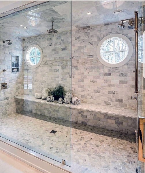 Spacious marble tile shower with bench seating, round windows, and rainfall showerhead.