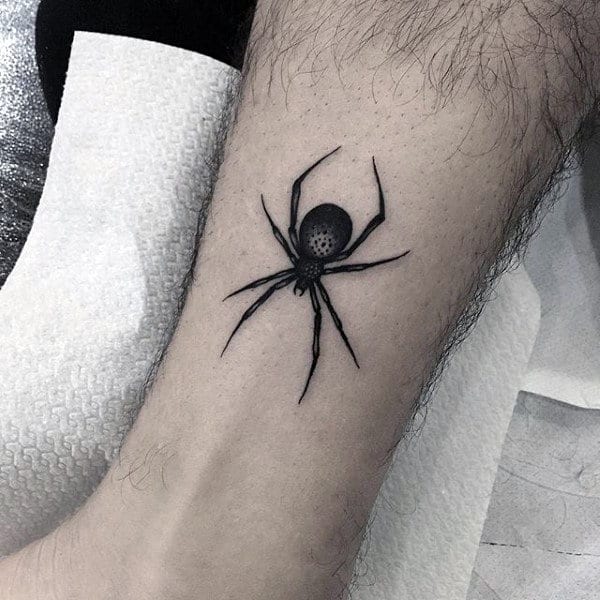 A black spider tattoo on the lower leg with paper laid beneath the leg