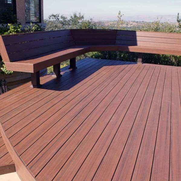 Wooden deck with a bench in the corner, offering views of trees and distant hills under a clear sky