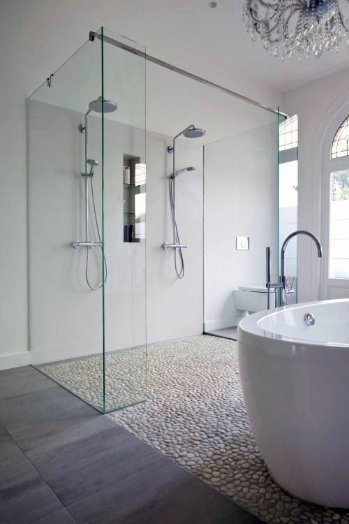 Large shower with double showerheads, glass enclosure, and pebble stone floor.