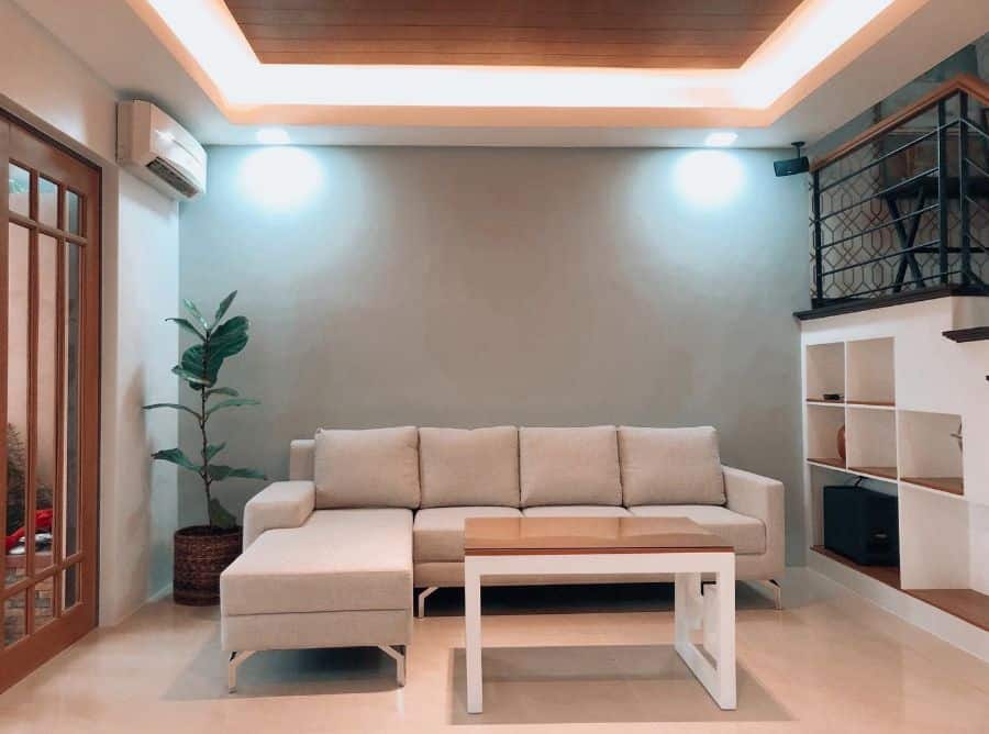 Living room with a beige sectional sofa, white coffee table, potted plant, and shelf unit under a staircase