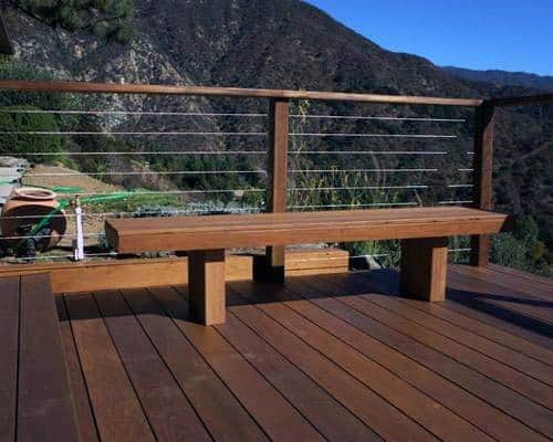 Wooden deck with a bench overlooking a mountainous forest under a clear blue sky