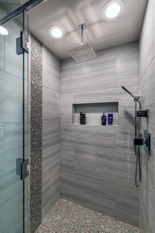 Large grey contemporary shower with pebble stone floor, recessed shelf, and rainfall showerhead.