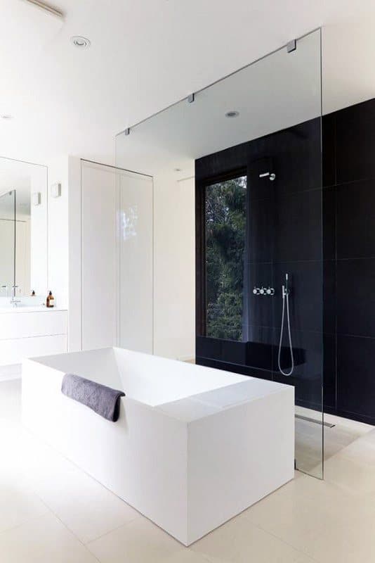 Minimalistic black and white bathroom with freestanding tub and glass shower partition.