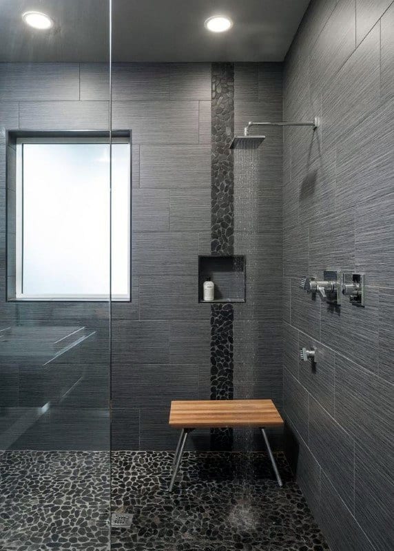 Large contemporary grey shower with pebble stone floor, built-in shelf, and wooden seat.