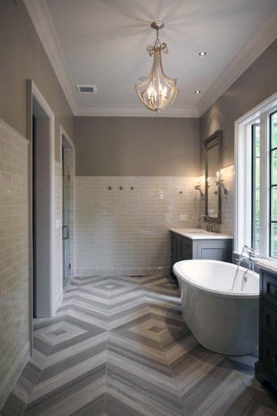 Bathroom with freestanding tub, chevron-patterned grey floor tiles, and chandelier lighting.