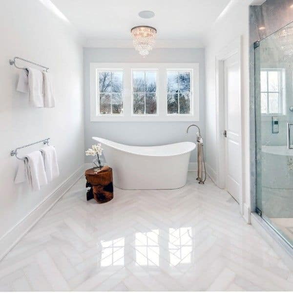 Large white bathroom with freestanding tub, glass shower, and polished chevron tile floor.