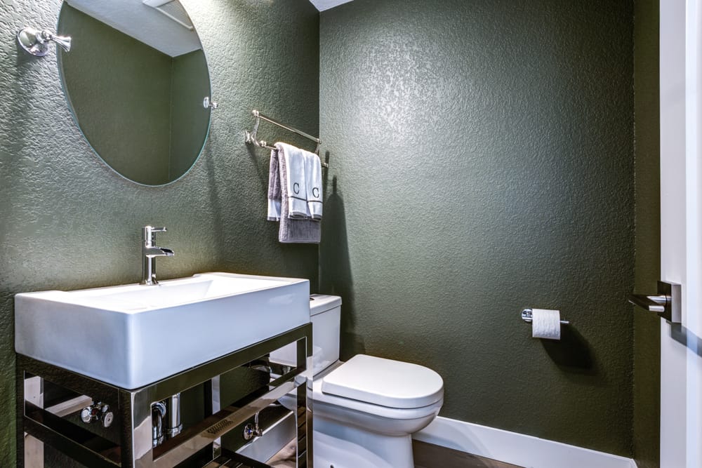 Modern bathroom with dark green walls, white vanity, and round mirror.