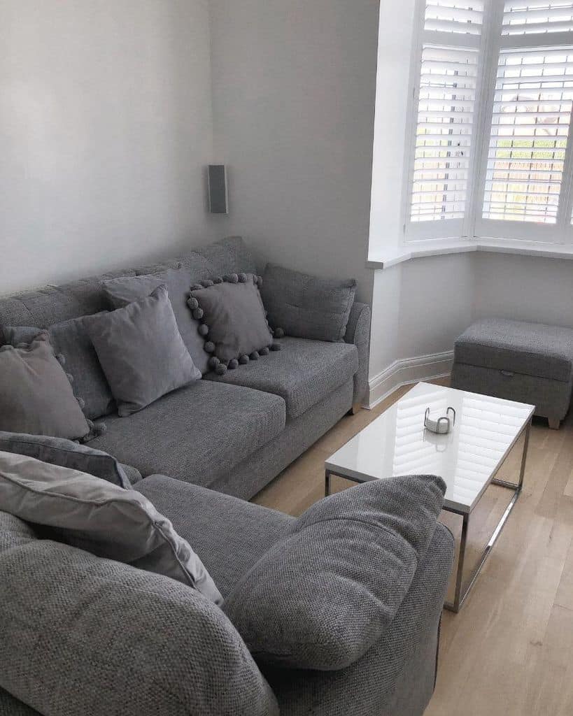 A cozy living room with a gray couch, matching pillows, a glass coffee table, and a window with blinds