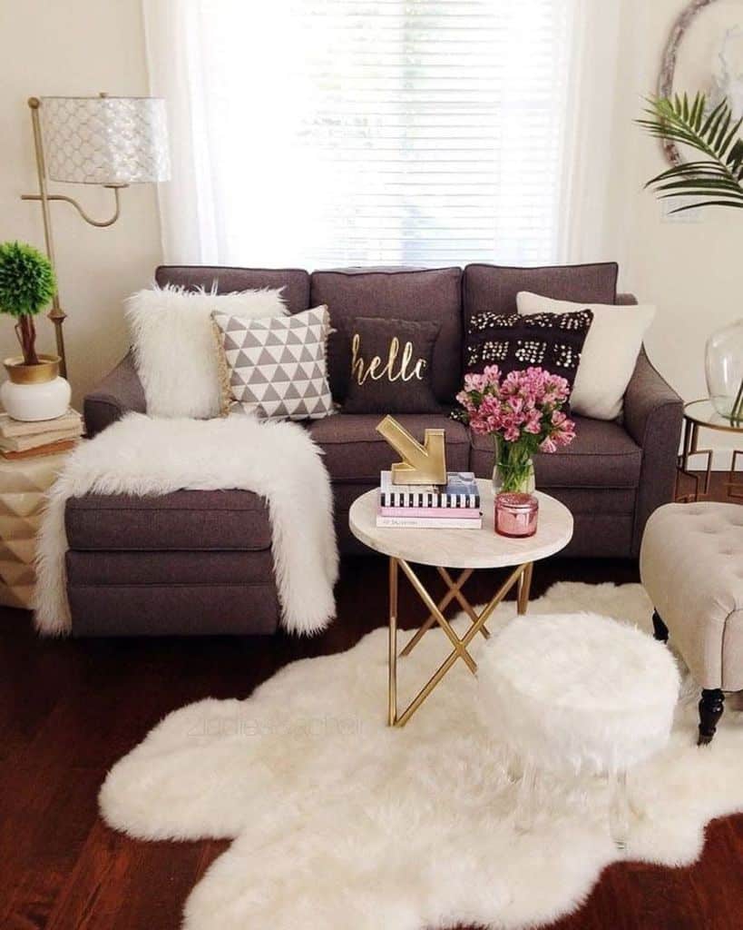 Cozy living room with a gray sofa, pillows, fluffy rug, side table with flowers, and modern decor accents