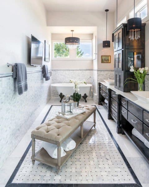 Elegant bathroom with freestanding bathtub, tufted bench, dark cabinets, and mosaic tile flooring.