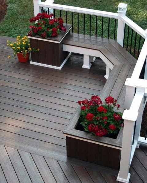 Wooden deck with built-in benches and planters, showcasing red and yellow flowers, enclosed by a white railing