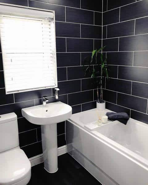 White bathtub and toilet with black tiled walls and pedestal sink.