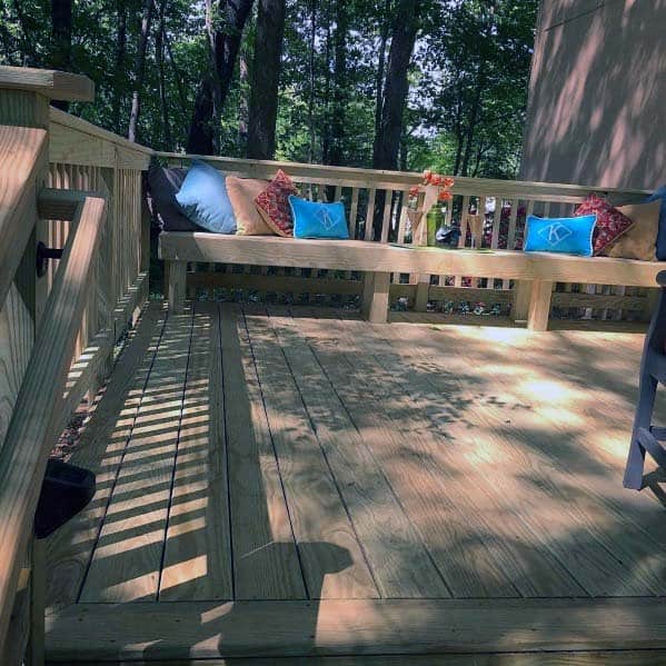 Wooden deck with a cozy bench, colorful cushions, and a lush forest backdrop