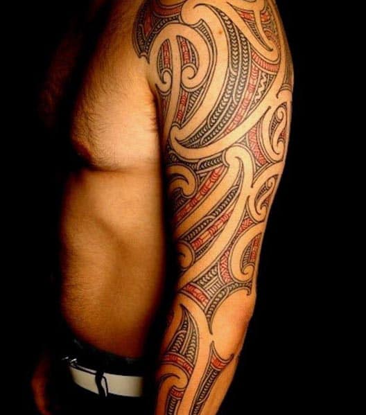 Man's arm and side torso with intricate tribal tattoo in black and red ink