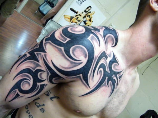 Close-up of a man's shoulder and chest with a large black tribal tattoo