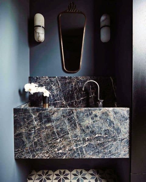 Marble vanity with geometric floor tiles and decorative mirror.