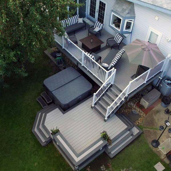 Elevated view of a backyard deck with seating, a bench, hot tub, stairs, umbrella, and lush greenery