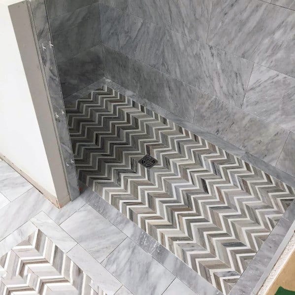 Shower with grey and white chevron-patterned floor tiles and marble walls.