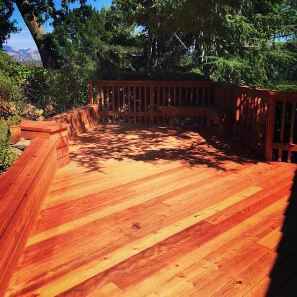 A wooden deck with a sunny view features a bench surrounded by trees and landscape in the background