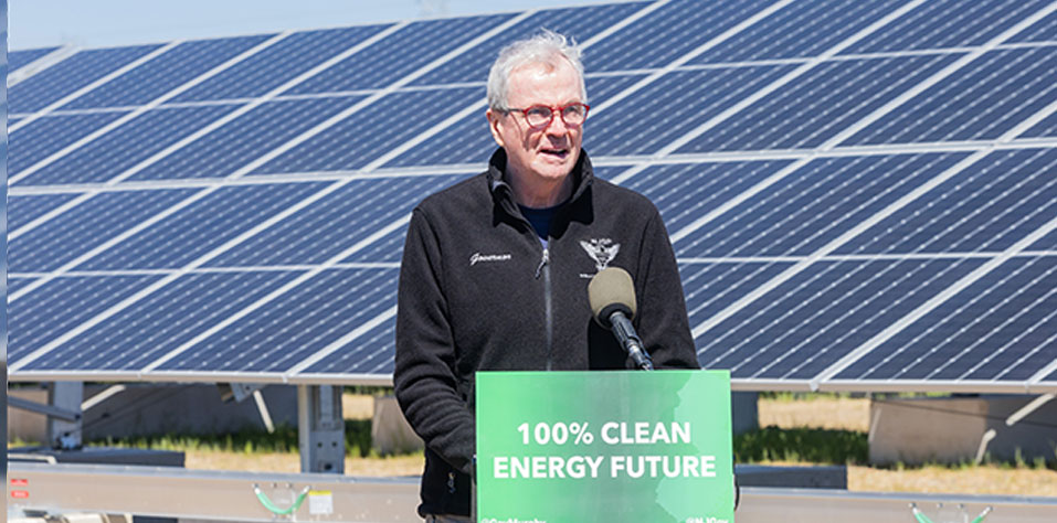 Governor standing, solar panels in the background, 100% clean energy sign